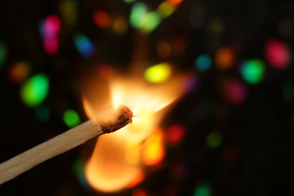 A striking image of a burning matchstick with vibrant, colorful bokeh in the background.
